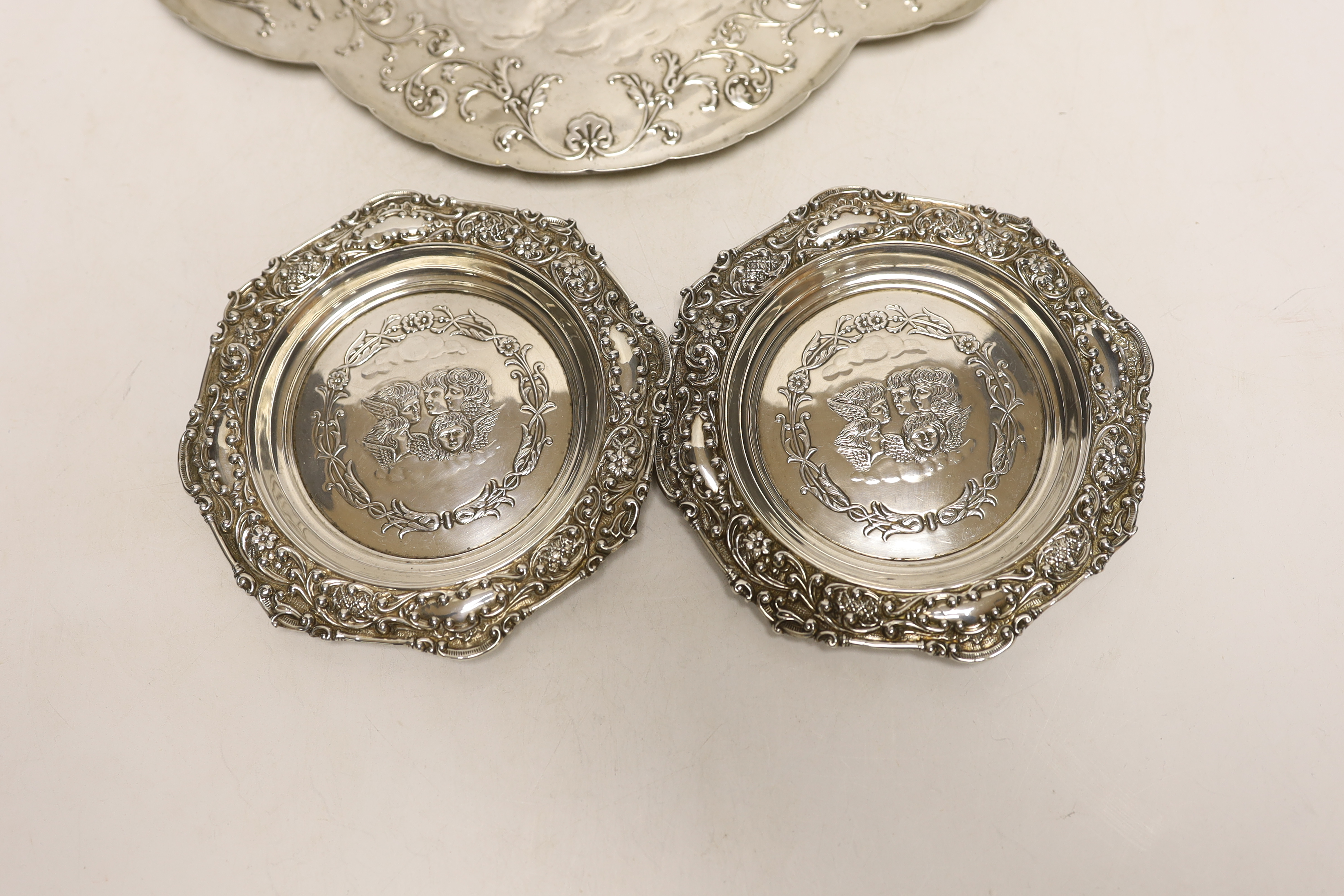 A late Victorian repousse silver dressing table tray with Reynold's Angels decoration, William Comyns, London, 1899, 30.9cm and a pair of smaller similar dishes by Henry Matthews, Birmingham, 1899, 14.2oz.